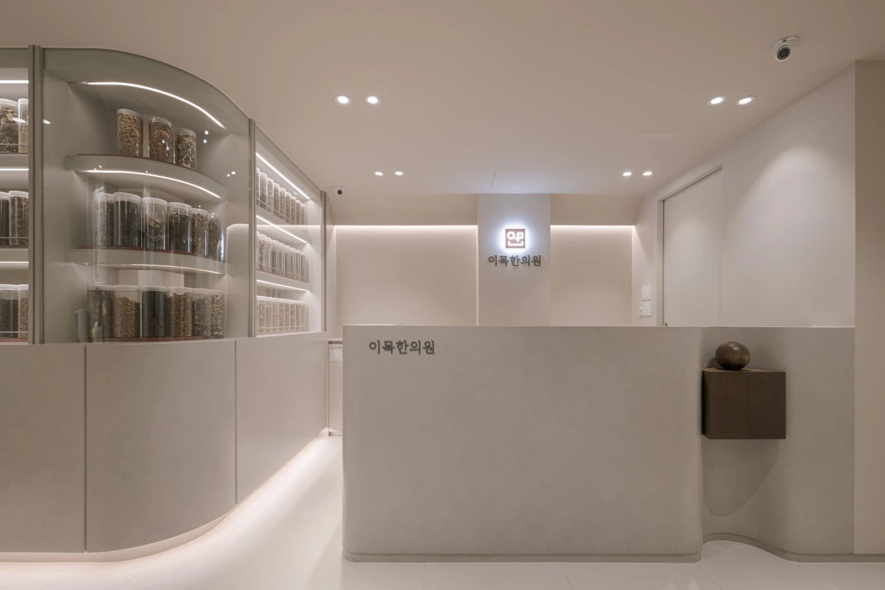 이목한의원 접수 데스크와 한약재 진열장이 보이는 내부 사진. 벽면 사인과 데스크에 이목한의원 표기